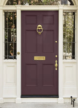 A classic six-panel front door in deep burgundy with polished gold hardware, including a knocker, letterbox, and handle, set within a white paneled entryway frame.